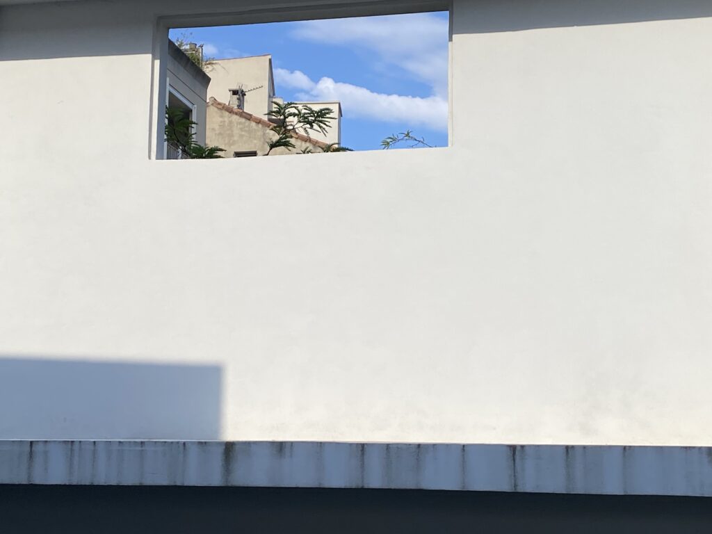 Un mur blanc.
Un silence.
Comme une page non écrite.

Et puis, une fenêtre.
Pas une échappée — une révélation.

Par l’ouverture,
un autre monde :
toits oubliés, ciel léger,
un fragment de réalité parallèle.

Chaque regard est une version.
Chaque cadre, un univers.

Nous vivons en multivers :
parfois mur,
parfois passage,
toujours multiples.
📸 Version courte pour Instagram :

Parfois, la vie ressemble à un mur.
Lisse, silencieux, bloqué.

Mais il suffit d’un cadre, d’une ouverture,
pour voir un autre monde apparaître. 🌍

Toits, ciel, verdure :
une version parallèle du réel.
Une autre vie, possible, là — juste derrière.

Multivers de la vie.
Multivers de soi.
Regarde autrement. ✨